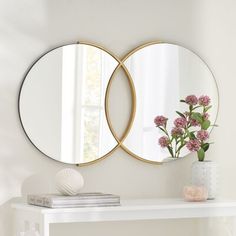 two round mirrors on the wall above a white table with pink flowers in vases