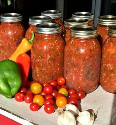 several jars filled with food sitting on top of a table next to tomatoes and peppers