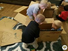 two young boys playing with cardboard boxes on the floor