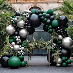 an arch made out of black, silver and green balloons