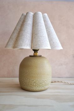 a table lamp sitting on top of a wooden table next to a pink wall with a white shade