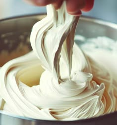 a person is mixing white cream in a metal bowl with a spoon on the side