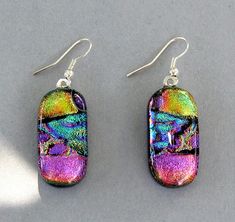 two pairs of earrings with multicolored glass and silver earwires on a gray surface