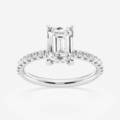 an emerald cut diamond engagement ring with diamonds on the band and side stones set in 18k white gold