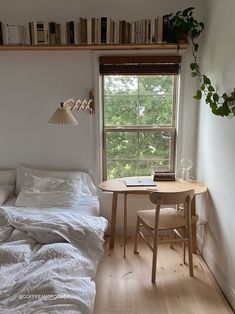 a small bedroom with a bed, table and bookshelf in the window sill