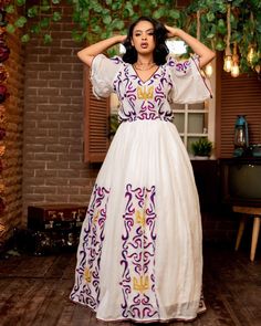 This stunning Habesha Kemis is a true work of art, featuring a mesmerizing Tilf pattern and the traditional elegance of the Shimena style. The intricate Tilf embroidery is expertly crafted, showcasing the beauty and richness of Ethiopian design. The flowing skirt and elegant neckline of the Kemis are designed to be both comfortable and flattering, making it the perfect choice for any special occasion. The vibrant colors of the Tilf pattern are both eye-catching and regal, adding to the overall b Resham Embroidered Dresses For Eid, Traditional Fitted V-neck Dress, White V-neck Dress With Resham Embroidery, Bohemian Ceremonial Dresses With Woven Motifs, Bohemian Cutdana Kaftan For Festivals, Maxi Length Kaftan For Wedding And Navratri, Wedding Kaftan For Navratri In Maxi Length, Traditional Floor-length Maxi Dress For Transitional Season, Festive Folk Dresses With Woven Motifs