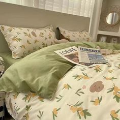 a bed with green and white sheets, pillows and a magazine on it's headboard