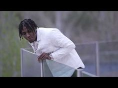 a man with dreadlocks leaning against a fence in the rain wearing a white suit