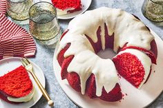 a red velvet bunt cake with white icing on a plate next to glasses