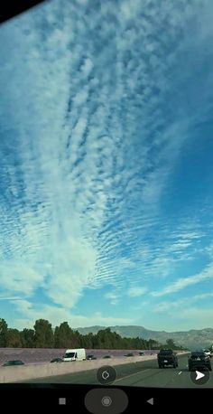 some cars driving down a highway under a blue sky with wispy white clouds