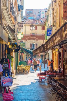 people are walking down an alleyway in the city with tables and chairs on either side