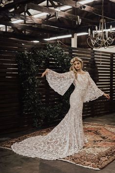 a woman standing on top of a rug wearing a white dress and holding her arms out