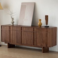 a wooden sideboard with two vases on it next to a lamp and other items