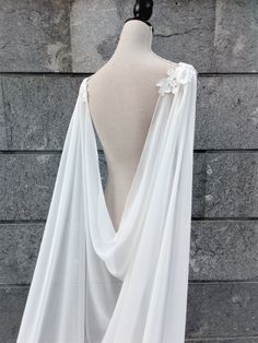 the back of a white dress on a mannequin's head stand in front of a stone wall