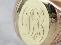 "Featuring components from different eras, this one-of-a-kind signet ring is a delightful combination of green and rose gold! The monogram at the center is beautifully engraved in ornate French script, while the ring's shoulders have subtle motifs that catch the light and shine. Please note that this signet ring has an original monogram, and unfortunately, this piece cannot be altered without affecting the quality of the piece. Please feel free to contact us to help you find your perfect signet Luxury Engraved Signet Ring Collectible, Collectible Yellow Gold Signet Ring With Engraving Option, Victorian Oval Signet Ring With Maker's Mark, Oval Engraved Signet Ring For Collectors, Luxury 14k Stamped Collectible Signet Ring, Luxury Round Signet Ring With Hallmarks, Oval Ring With Maker's Mark For Gift, Victorian Round Signet Ring With Engraving Option, 14k Gold Engraved Ring With Initials For Collectors