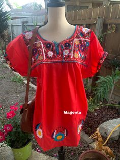 a woman's red top with colorful embroidered designs on the chest and shoulder, hanging from a mannequin