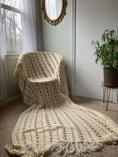 a white crocheted blanket sitting on the floor next to a potted plant