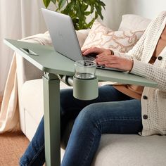 a woman sitting on a couch using a laptop computer with a cup of coffee in front of her