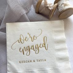 a napkin with the words we're engaged written on it next to a pair of shoes