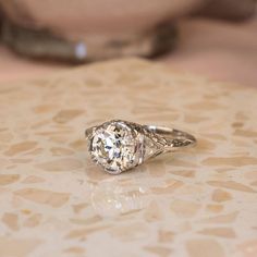 an old - fashioned diamond ring sits on a marble table with a woman's hand in the background