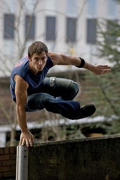 a man on a skateboard does a trick over a rail in front of a building