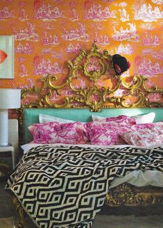 a bed with pink and gold decor in a room that has orange wall paper on the walls