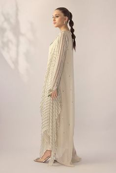 An ivory georgette long shirt with a draped dupatta is handworked with delicate kamdani. The sleeves and neckline are detailed with jewelled floral motifs. An elegant ensemble for any formal event or soiree. Designer Wear Draped Dupatta With Mirror Work, Designer Draped Dupatta With Mirror Work, Georgette Dresses With Resham Embroidery And Cape Sleeves, Designer Mirror Work Draped Dupatta, Draped Georgette Dress With Sheer Dupatta, Elegant Draped Designer Dresses, Elegant Draped Dress With Dupatta, Off White Dupatta With Mirror Work, Traditional Drape, Elegant Off White Kurta With Dupatta