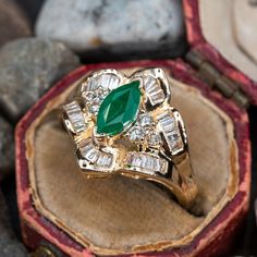 This elegant ring is centered with one (1) marquise cut natural emerald set into a two-prong setting. The emerald is bordered with six (6), prong set, round brilliant cut diamonds and thirty (30), channel set, baguette cut diamonds. The ring measures 16.0mm at the top, rises 7.8mm above the finger, tapering to 2.0mm wide and 1.1mm thick at the base of the shank. This ring is currently a size 6.75. There is a faint surface line inclusion on the emerald. Luxury Yellow Gold Emerald Ring Marquise Cut, Luxury Yellow Gold Emerald Ring With Intricate Design, Heirloom Marquise Emerald Ring, Heirloom Marquise Birthstone Ring For Anniversary, Marquise Emerald Ring In Yellow Gold, Marquise Emerald Ring In Gold, Emerald Ring With Marquise Cut Diamond Center Stone, Formal Marquise Yellow Gold Emerald Ring, Heirloom Marquise Emerald Ring In 14k Gold