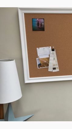 a cork board with pictures and photos on it next to a lamp, framed photograph