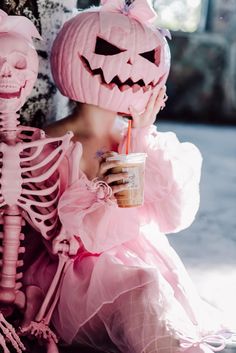 a woman in pink dress sitting next to a skeleton holding a drink and looking at the camera