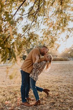 a man and woman kissing under a tree in an open field with leaves on the ground