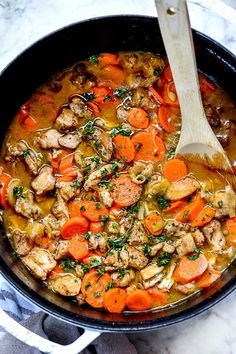 a pot filled with meat and carrots next to a wooden spoon