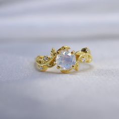 a gold ring with an opal surrounded by small white diamonds on a white cloth