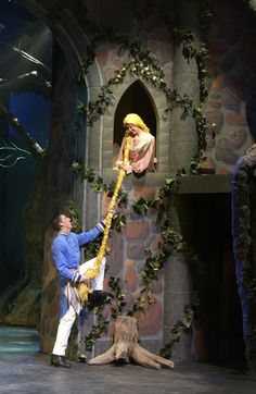 two people are performing on stage in front of a fake man with a yellow scarf