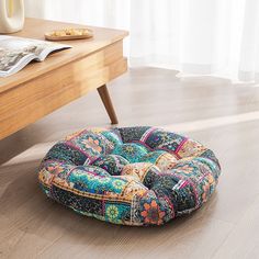 a multicolored round floor pillow sitting on the floor in front of a wooden table