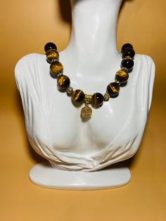 Add a touch of elegance to your outfit with this stunning gemstone necklace designed for women. Featuring 16mm Tigers Eye gemstone beads adorned with a beautiful gold-plated crystal flower wheel, this necklace is perfect for adding a pop of color and sophistication to any look. Handcrafted with precision and attention to detail, this unique piece is sure to make a statement wherever you go. this necklace exudes charm and sophistication. Perfect for everyday wear or special occasions, this piece Elegant Natural Stone Necklaces For Meditation, Elegant Necklaces With Natural Stones For Meditation, Beaded Round Pendant Necklaces For Healing, Amber Beaded Necklace With Large Beads As Gift, Gold Necklaces With Round Stone Beads, Elegant Gemstone Beads In Gold, Elegant Amber Jewelry With Polished Beads, Agate Gemstone Beads Necklaces, Meditation Necklaces With Round Beads And Stones