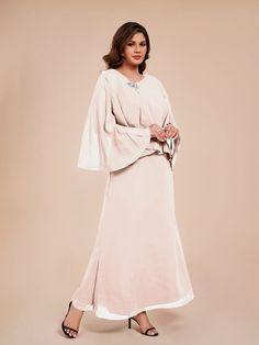 a woman in a long dress with cape sleeves and high heels standing on a beige background