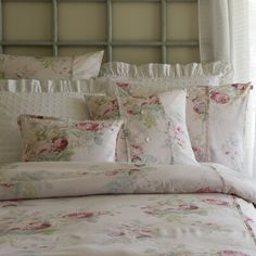 a white bed with pink flowers and ruffled trimmings on the headboard