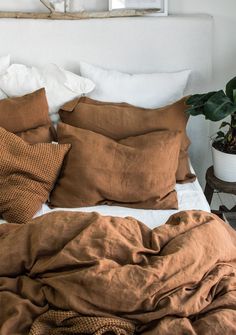 an unmade bed with brown linens and pillows on it, next to a potted plant