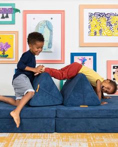 two children playing on a blue couch in a living room with colorful pictures on the wall