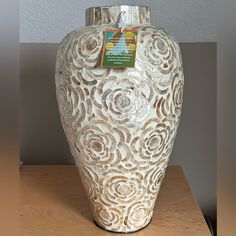 a white vase sitting on top of a wooden table next to a light colored wall