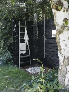 an outdoor shower in the woods next to a tree and some bushes with towels hanging on it