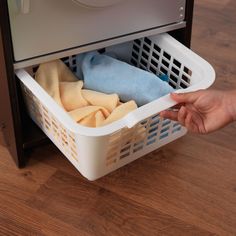 a person holding a basket with clothes in it on top of a wooden floor next to a washer and dryer