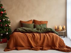 a bed with orange sheets and green pillows next to a christmas tree in a room