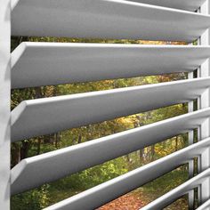 an open window with white blinds in front of trees and leaves on the outside wall