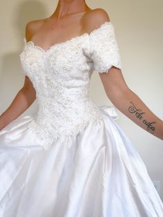 a woman in a white wedding dress with tattoos on her arm