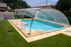 an in ground swimming pool with a glass cover on the side and grass around it