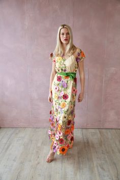 a woman standing in front of a pink wall wearing a dress with flowers on it