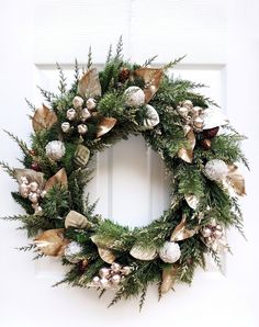 a christmas wreath hanging on the front door with ornaments and greenery all around it