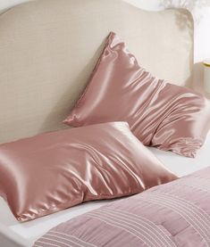 a bed with pink sheets and pillows on top of the headboard, next to a night stand